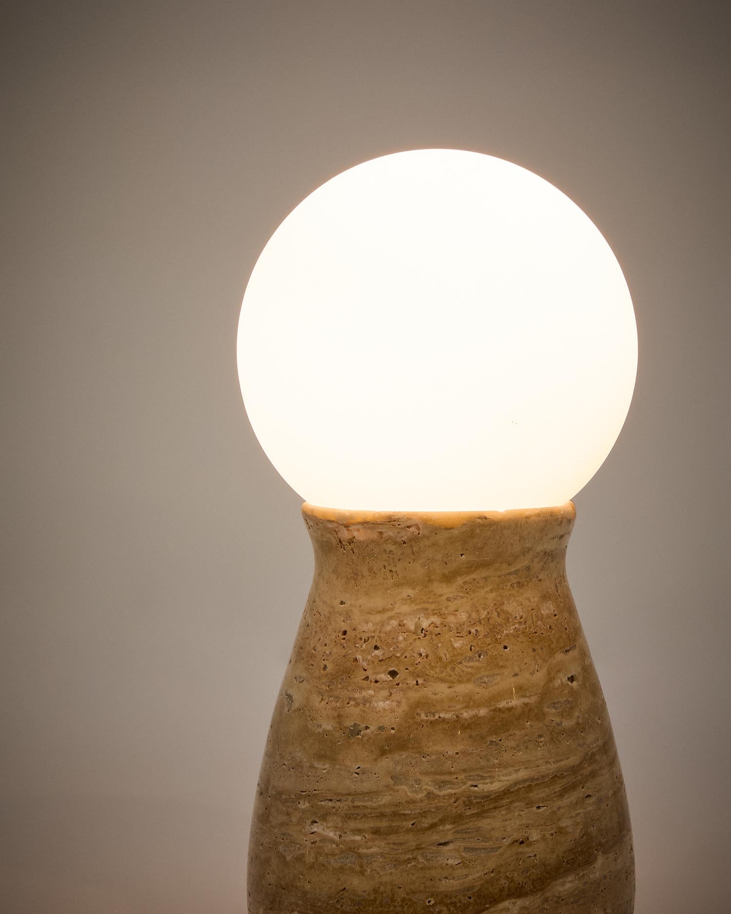 Die Tischleuchte Okeni von Kave Home kombiniert edlen Travertin mit elegantem Glas und schafft so eine stilvolle Atmosphäre in Ihrem Zuhause.