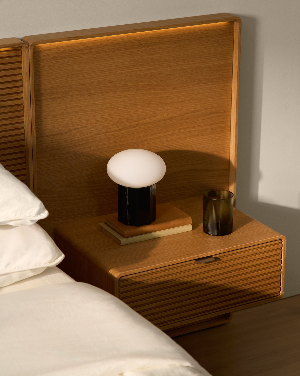 Bett Norlen aus Eichenfurnier mit abgerundetem Kopfteil, horizontaler Linienfräsung, LED-Lichtband und zwei passenden Nachttischen.