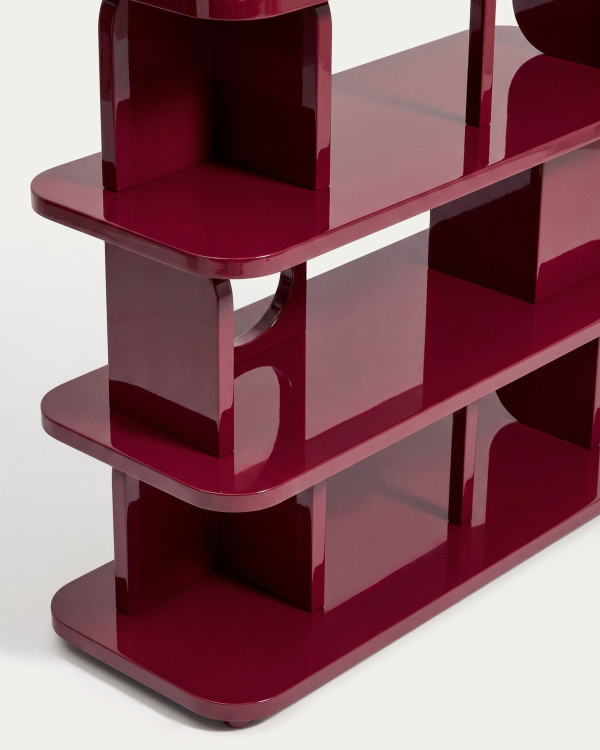 Freistehendes Regal aus MDF und Buchenholz in glänzendem Granatrot, mit geometrischen Aussparungen und mehreren übereinander liegenden Ablageflächen.