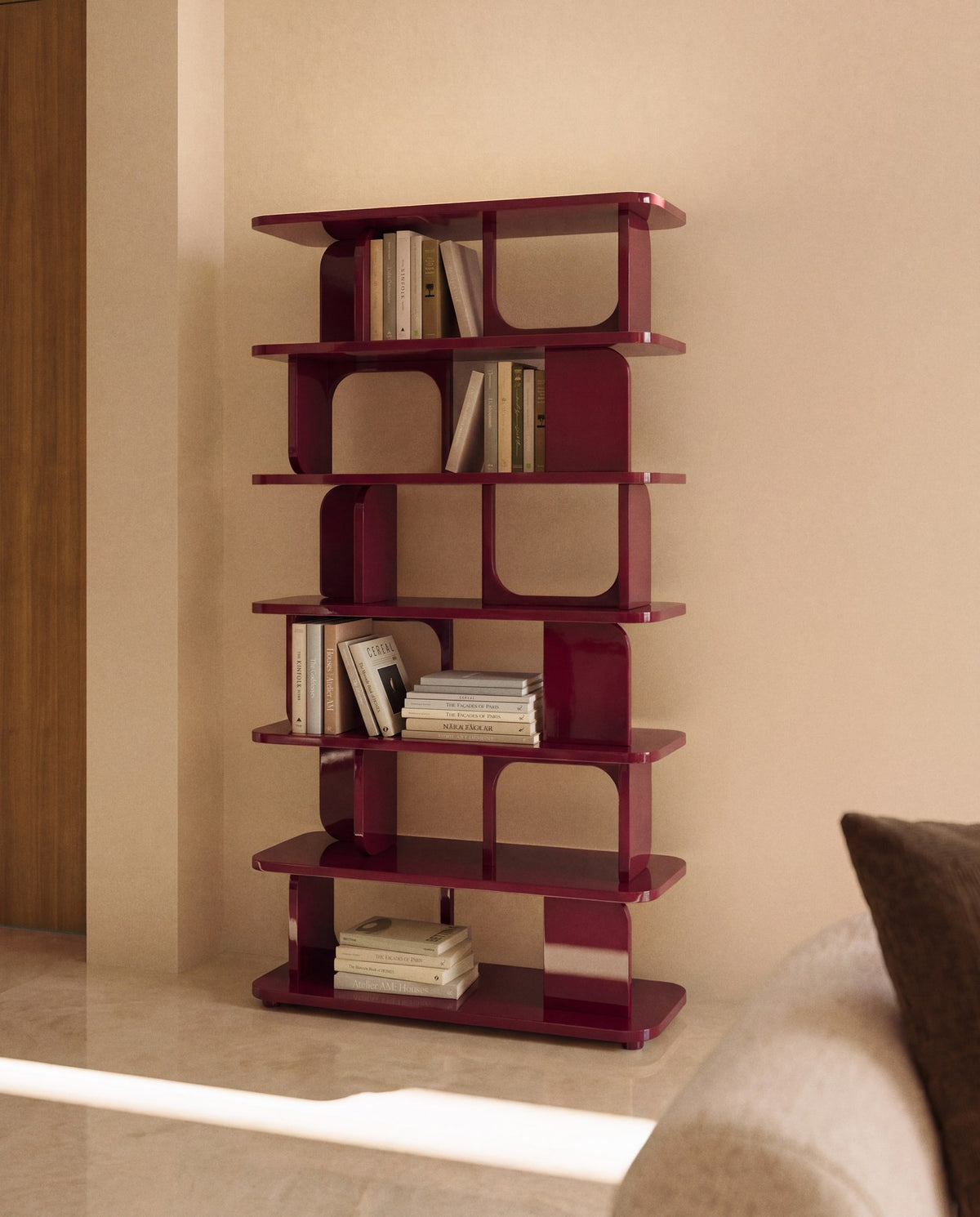 Freistehendes Regal aus MDF und Buchenholz in glänzendem Granatrot, mit geometrischen Aussparungen und mehreren übereinander liegenden Ablageflächen.