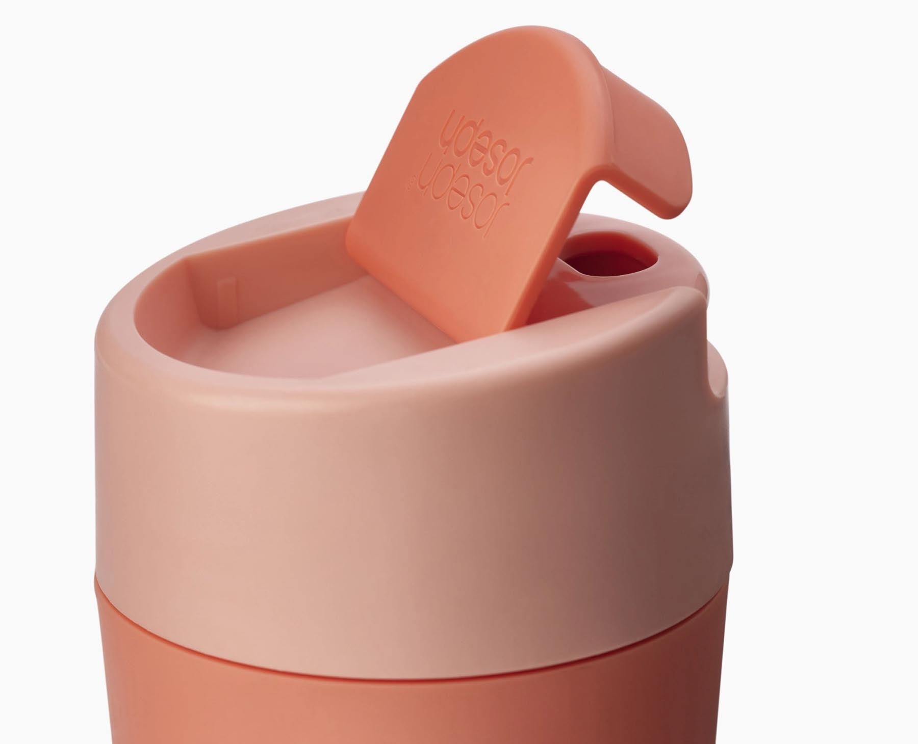 Praktischer Sipp Reisebecher in leuchtendem Koralle, ideal für Reisen. Ausgestattet mit einem cleveren Klappdeckel für einfaches Trinken.