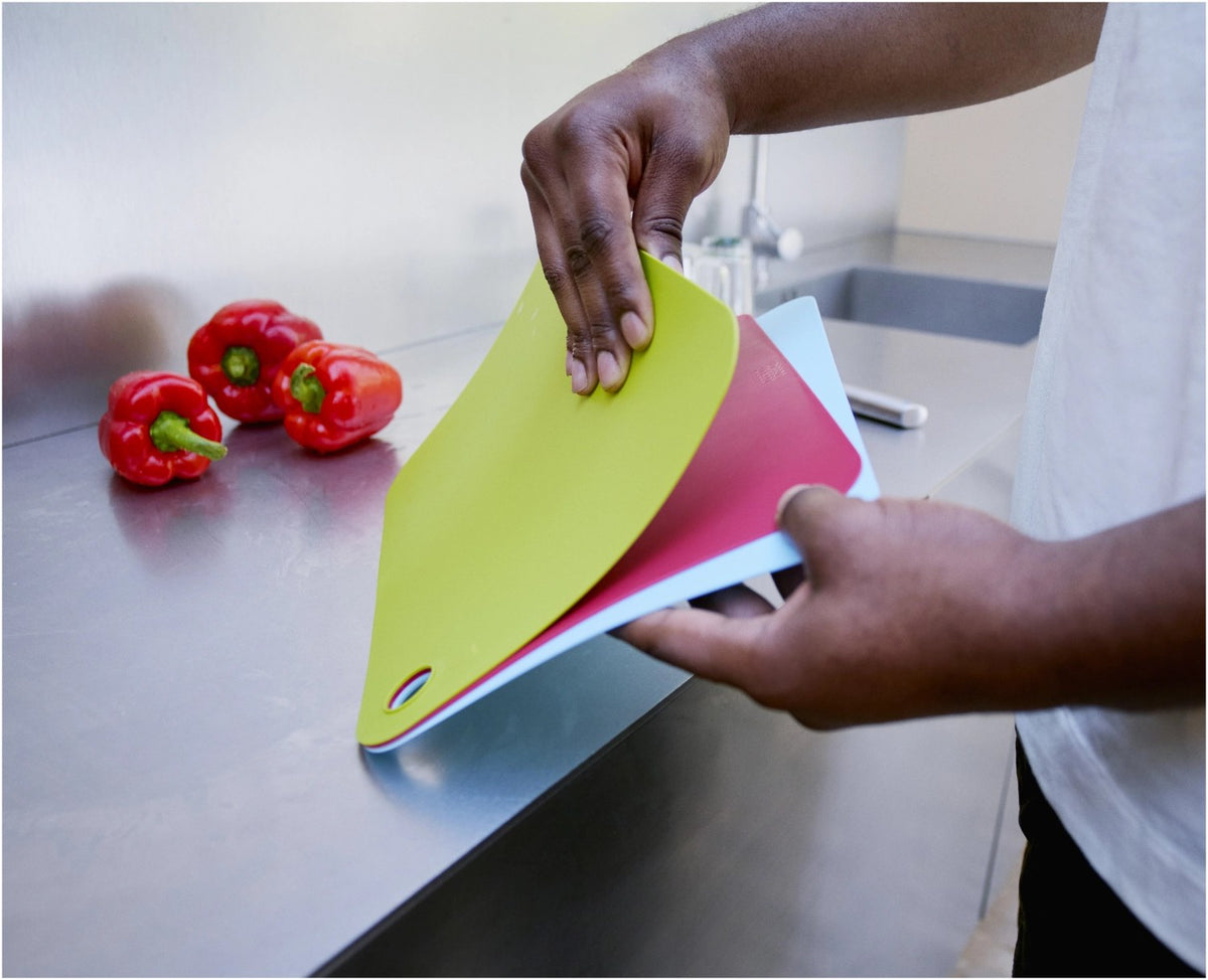 Drei bunte, kompakte Kunststoff-Schneidematten im Set, mit beidseitiger Schneidfläche und Klipp-Verschluss zur platzsparenden Aufbewahrung, Marke Joseph Joseph.