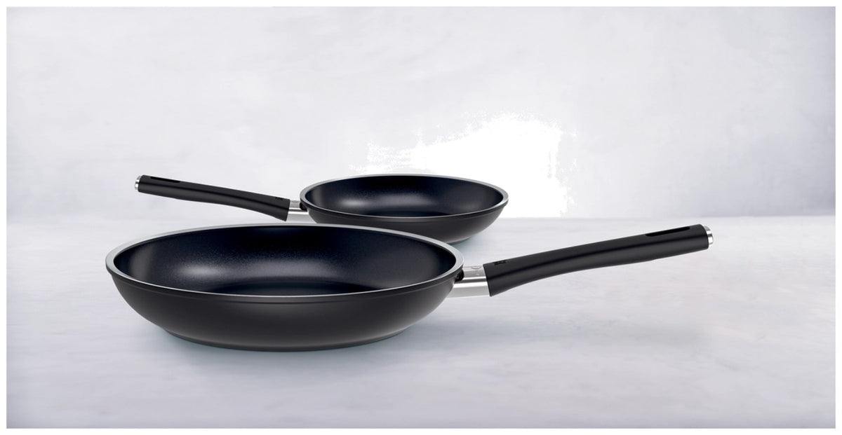 Zwei schwarze Bratpfannen aus Aluminium in den Grössen 24 und 28 cm mit Keramikbeschichtung und Griff, nebeneinander auf einer Fläche fotografiert.