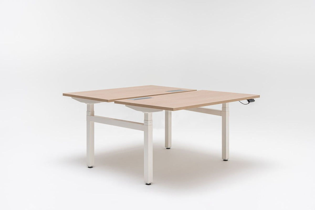 Doppelschreibtisch Ogi Drive Bench in Honigeiche mit schwarzem Metallgestell, zwei Teleskopsäulen und Bedienfeldern für Höhenverstellung.