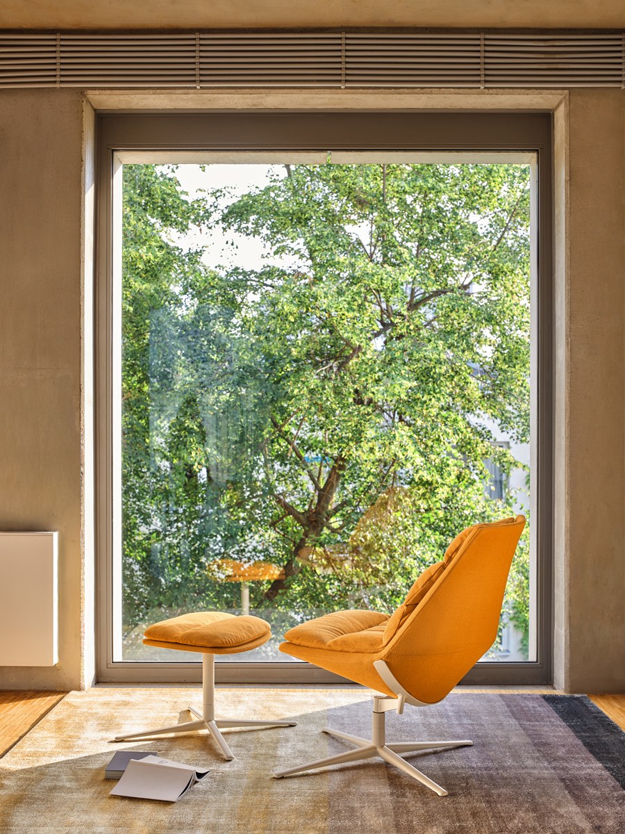 Ziegelroter Loungesessel mit gepolstertem Sitz, drapiertem Kissen und Aluminium-Drehfuss auf vier Sternbeinen, Frontalansicht.
