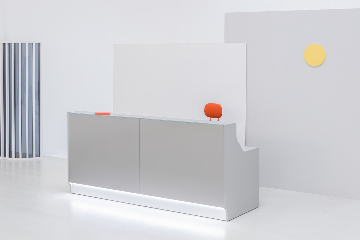 Weisse modulare Empfangstheke Linea von Mdd mit Glasfront, LED-Beleuchtung, Aluminiumsockel und Edelstahl-Eckleiste im Büro.