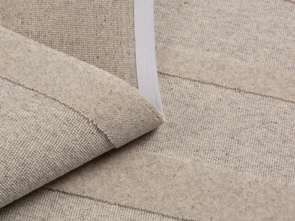 Hellgrauer rechteckiger Teppich Archipelagio von Micadoni aus 100% Wolle mit dichtem Flor und sauber verarbeiteten Kanten auf hellem Boden.