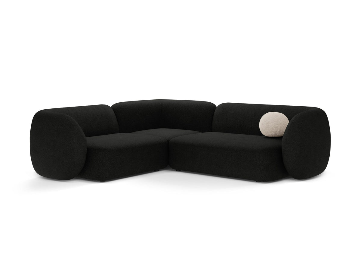 Weisses Ecksofa links Kate von Micadoni mit Bouclé-Stoff Baloo, schwarzen Kunststoffbeinen und niedriger Rückenlehne im Wohnraum.