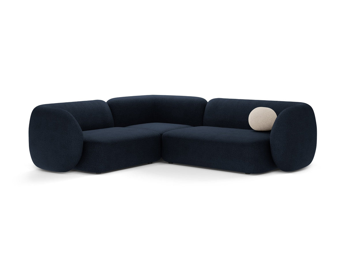 Weisses Ecksofa links Kate von Micadoni mit Bouclé-Stoff Baloo, schwarzen Kunststoffbeinen und niedriger Rückenlehne im Wohnraum.