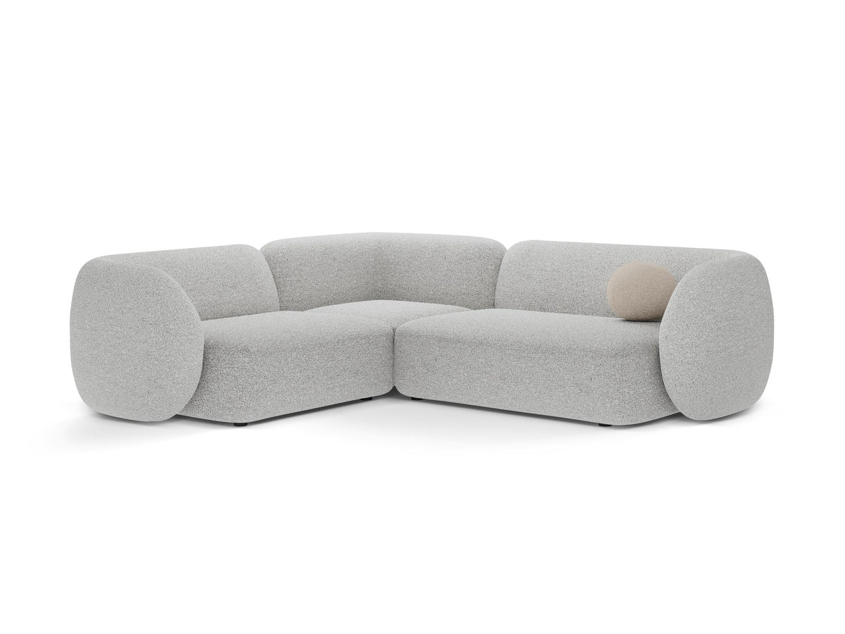 Weisses Ecksofa links Kate von Micadoni mit Bouclé-Stoff Baloo, schwarzen Kunststoffbeinen und niedriger Rückenlehne im Wohnraum.