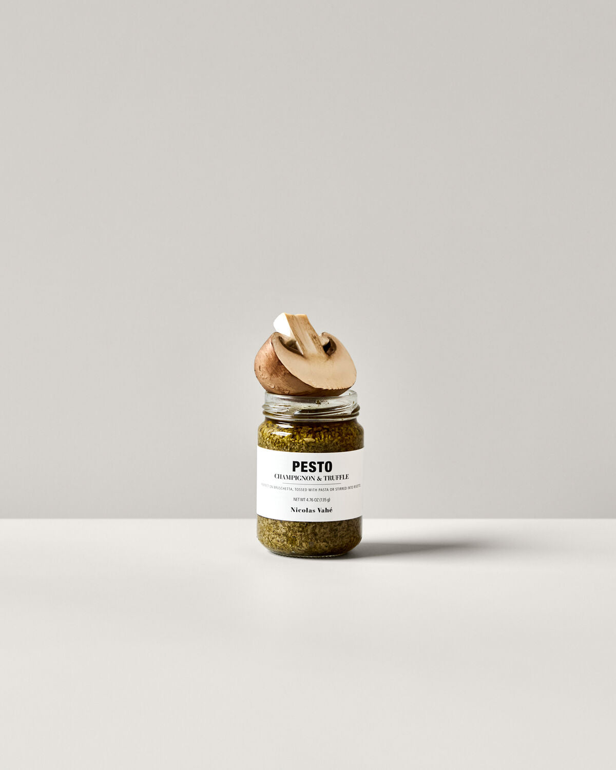 Ein Glas Pesto mit Champignons und Trüffel von Nicolas Vahé, 135 g, stilvoll präsentiert auf einem Holzbrett mit frischen Zutaten.