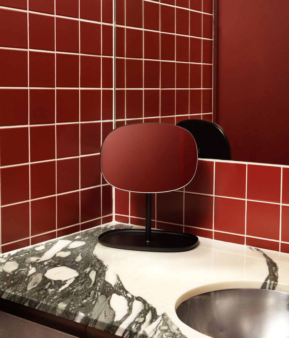 Tischspiegel Flip von Normann Copenhagen mit rundem Glasspiegel und Fuss aus beschichtetem Stahl in organischer Form, Farbe Schwarz.