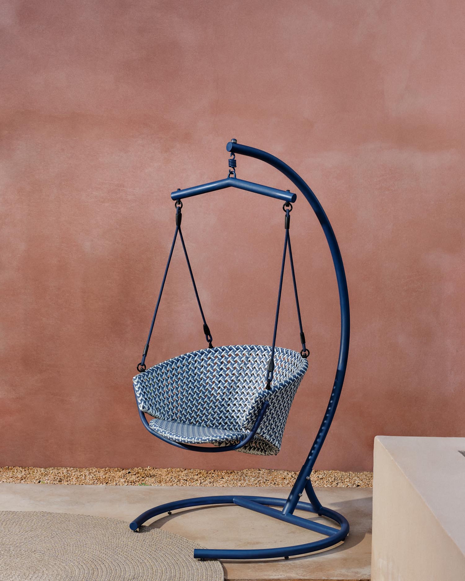 Eleganter Hängesessel aus Aluminium und blauem Rattan, robust, pflegeleicht, mit Fußteil für maximalen Komfort.