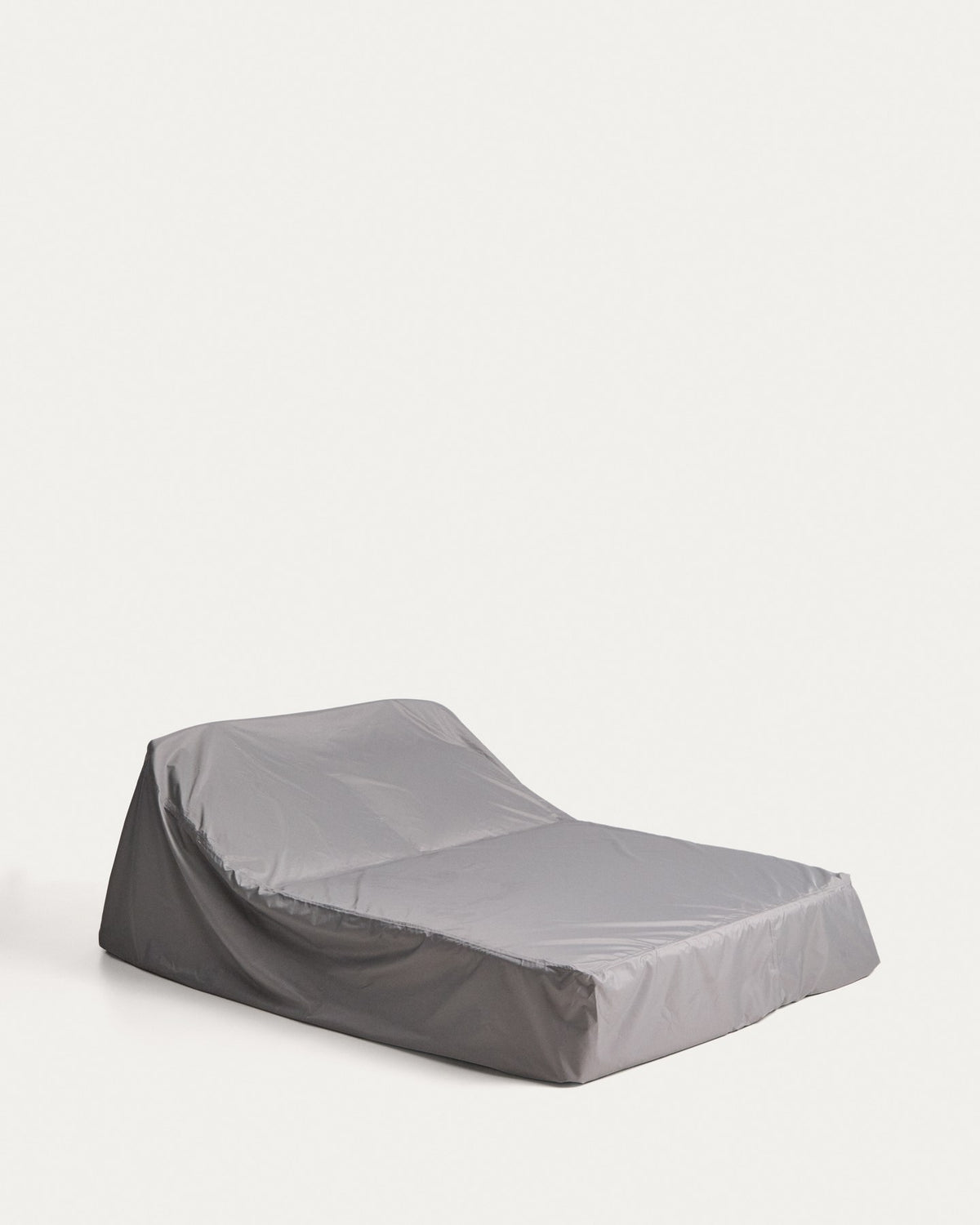Graue Schutzhülle aus Polyester für Outdoor-Möbel, mit verschweissten Nähten und Belüftungsfenster, auf einer Sonnenliege drapiert.