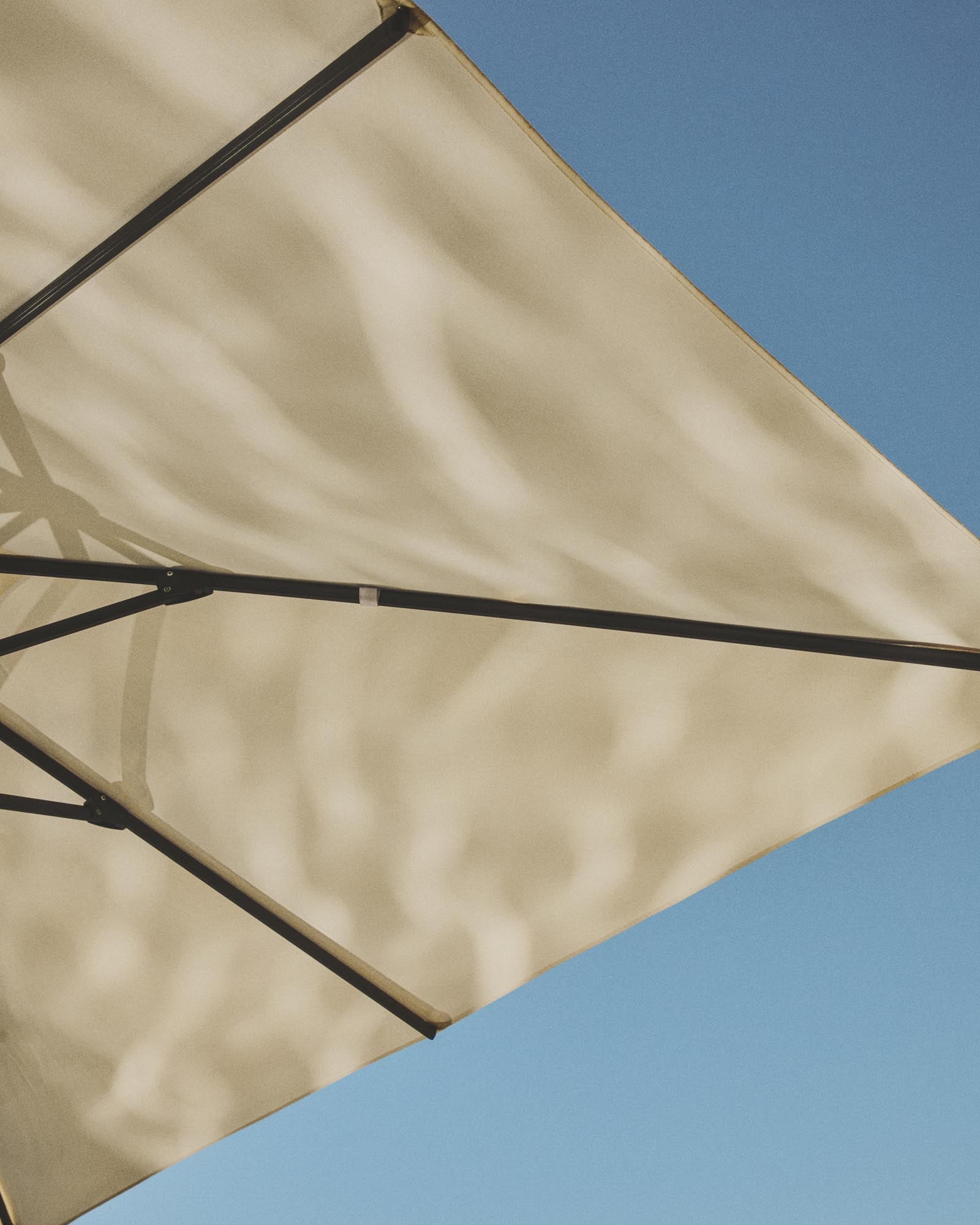 Exzentrischer Sonnenschirm Noli in warmem Beige, ausgestattet mit einem stabilen taupefarbenen Aluminiumgestell, perfekt für entspannte Sommertage.