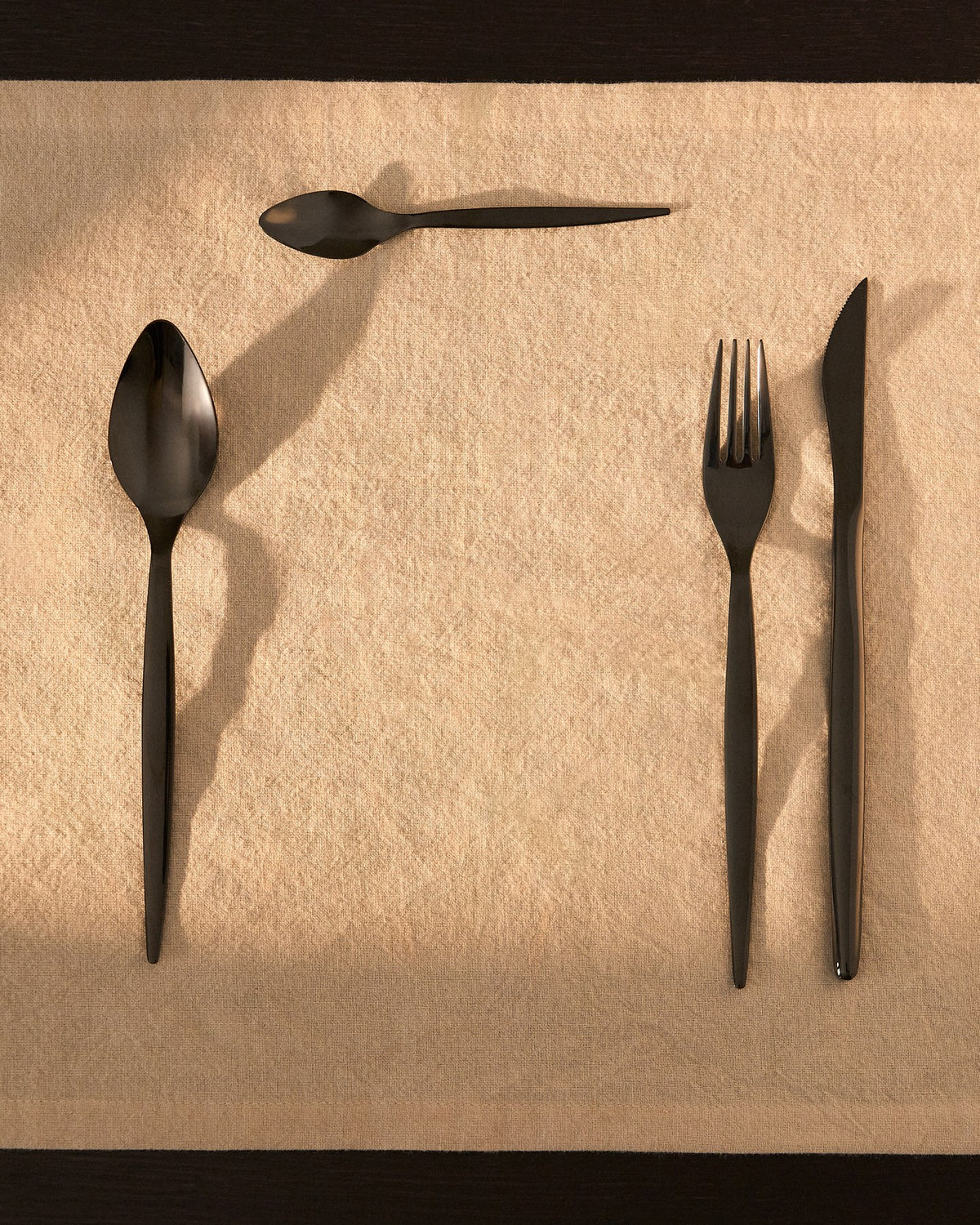 Foto eines 16-teiligen Besteckset aus Edelstahl mit glänzend schwarzem Finish, bestehend aus Messern, Gabeln und Löffeln.