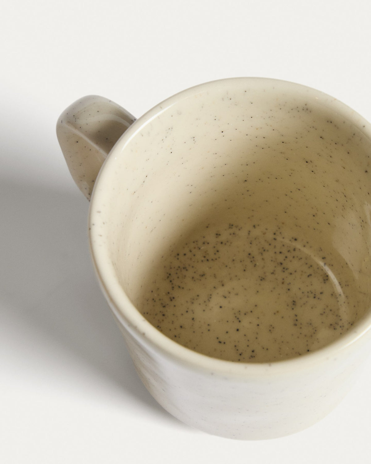 Weisse Tasse Daner aus glänzender Keramik mit schlichter, runder Form und leicht beiger Färbung, fotografiert vor neutralem Hintergrund.
