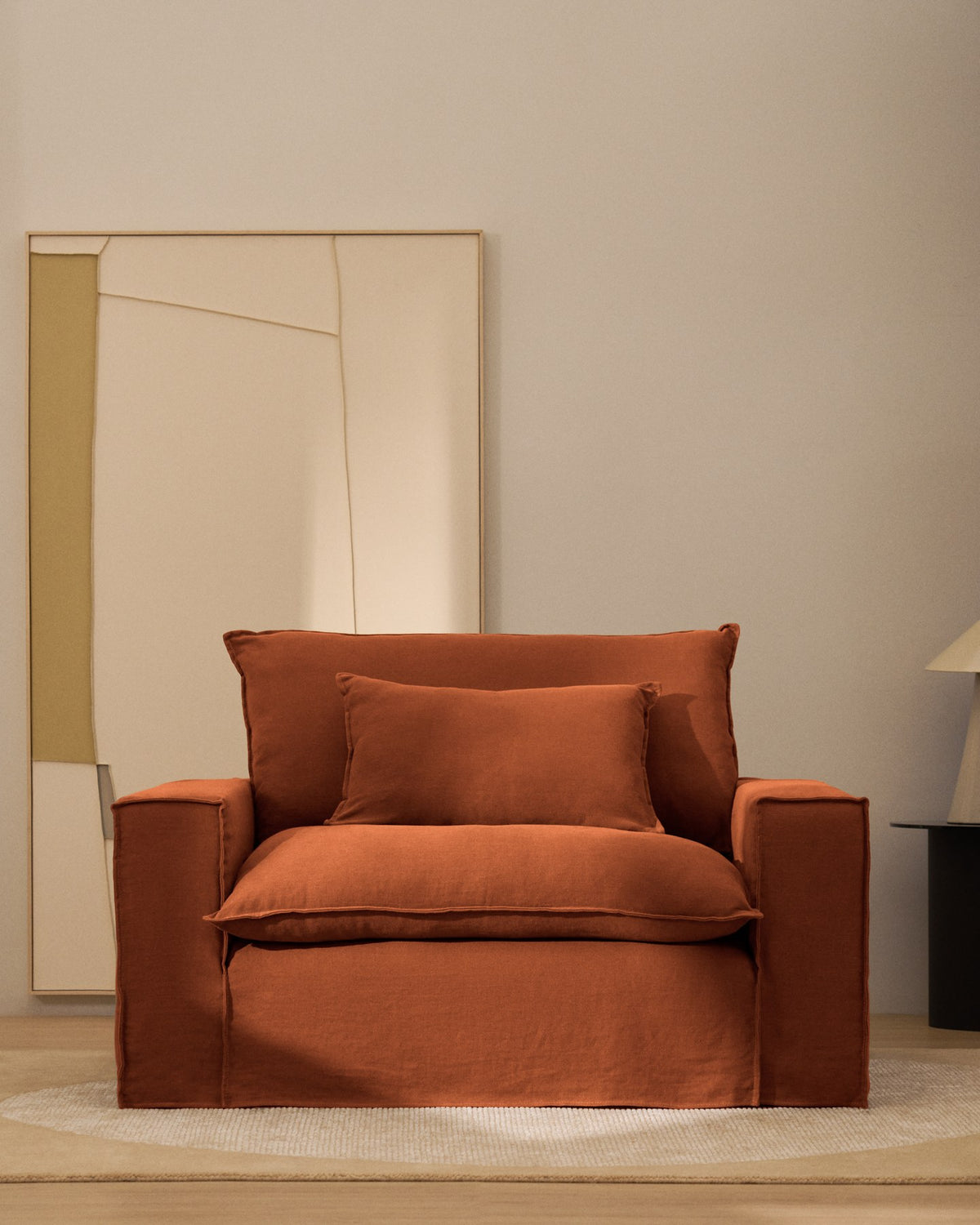 Terrakottafarbener Sessel Anarela mit abnehmbarem Leinenbezug, schwarzen Kunststoffbeinen und gepolsterter Sitzfläche, Breite 150 cm.