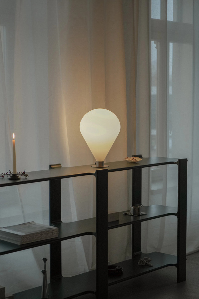 Elegante Ely ELY01 Tischleuchte von Tamo, harmonisch auf einem modernen Tisch arrangiert, vereint Metall und Glas für ein warmes Lichtspiel.