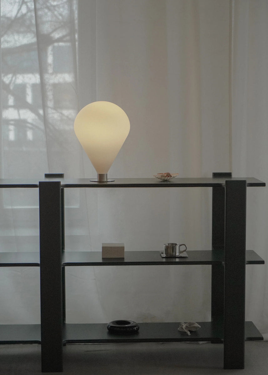 Stilvolle Ely ELY01 Tischleuchte von Tamo, präsentiert auf einem zeitgenössischen Tisch, kombiniert edles Metall und Glas für eine gemütliche Atmosphäre.