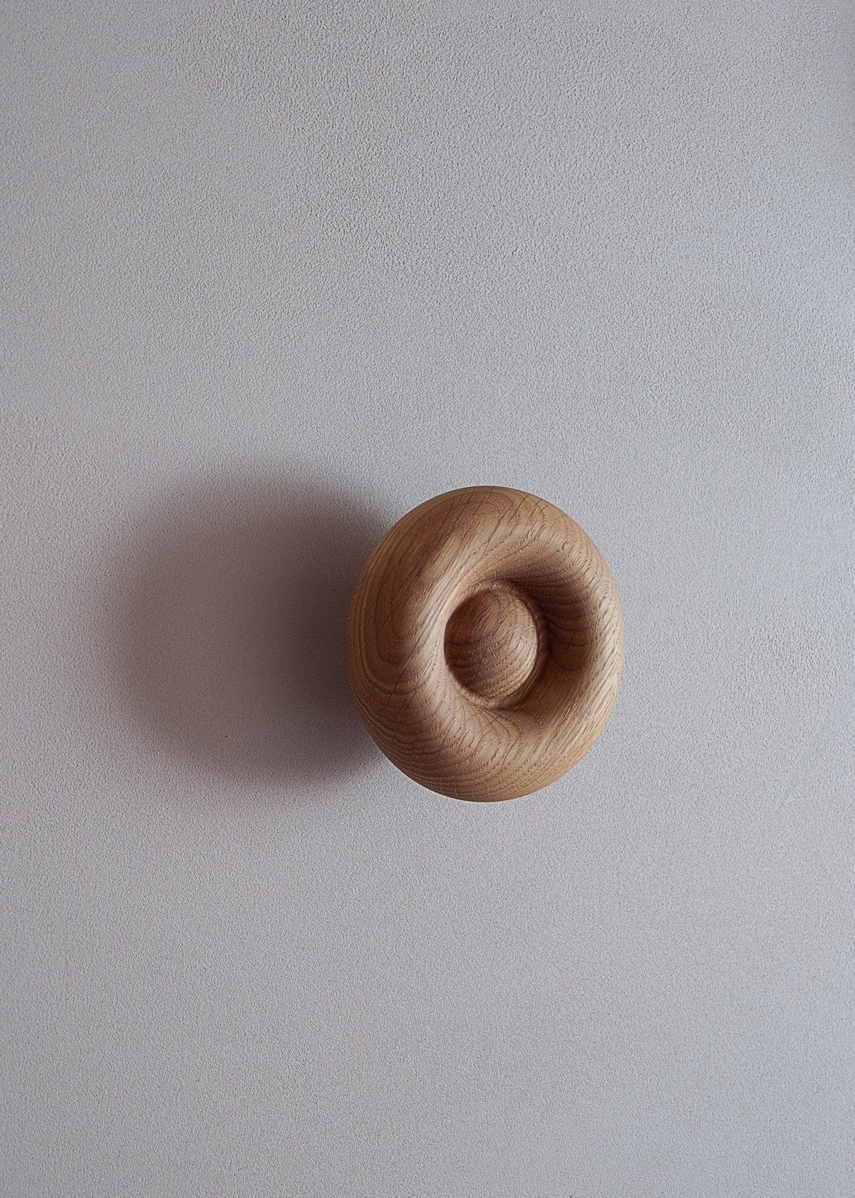 Blop Kleiderhaken von Tamo aus geöltem Massivholz in Esche, runde organische Form, an weisser Wand montiert, natürliche Maserung sichtbar.