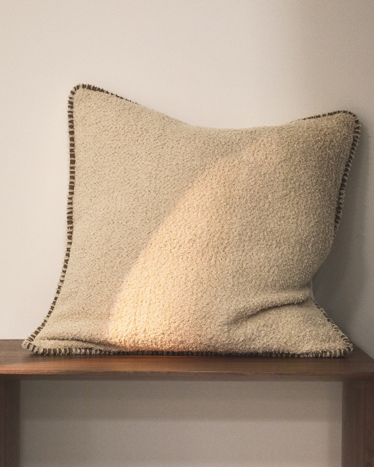 Beige quadratischer Kissenbezug aus Baumwoll-Bouclé-Gewebe mit brauner Kontrastpaspel am Rand, Grösse 50 x 50 cm, Nahaufnahme der Textur.