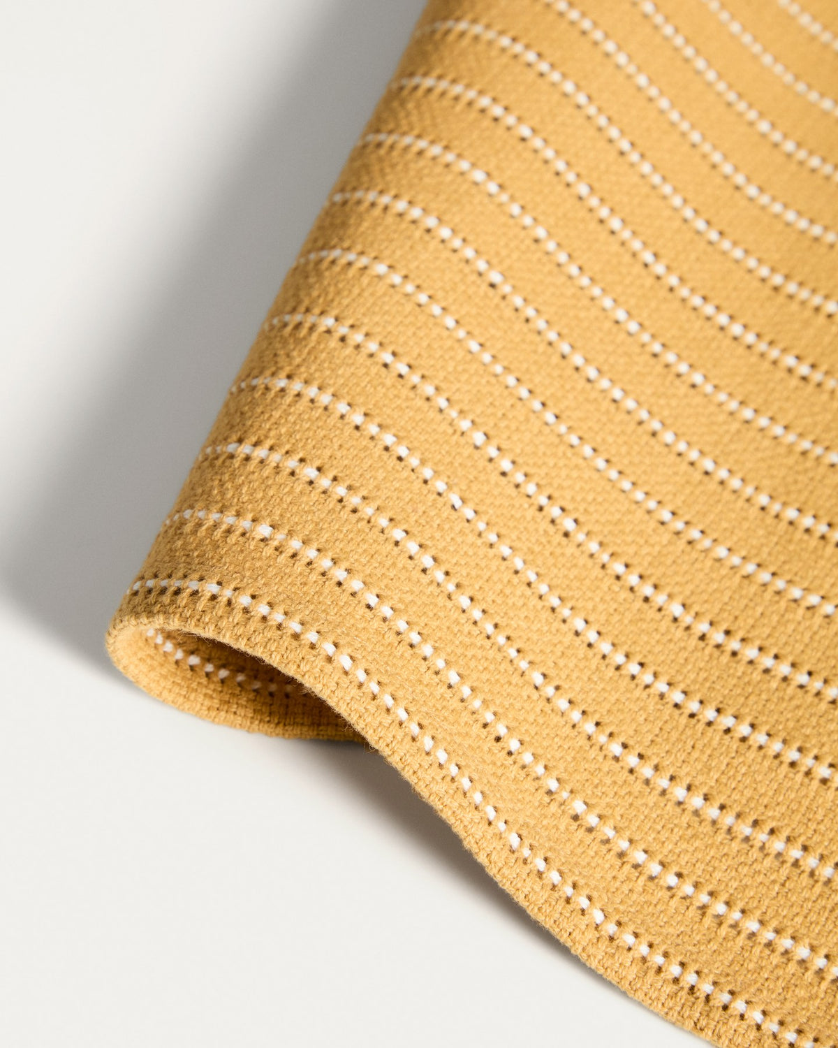 Zwei senfgelbe Tischsets aus Baumwolle mit eingewebtem Jacquard-Muster, rechteckige Form, auf einem Tisch platziert.