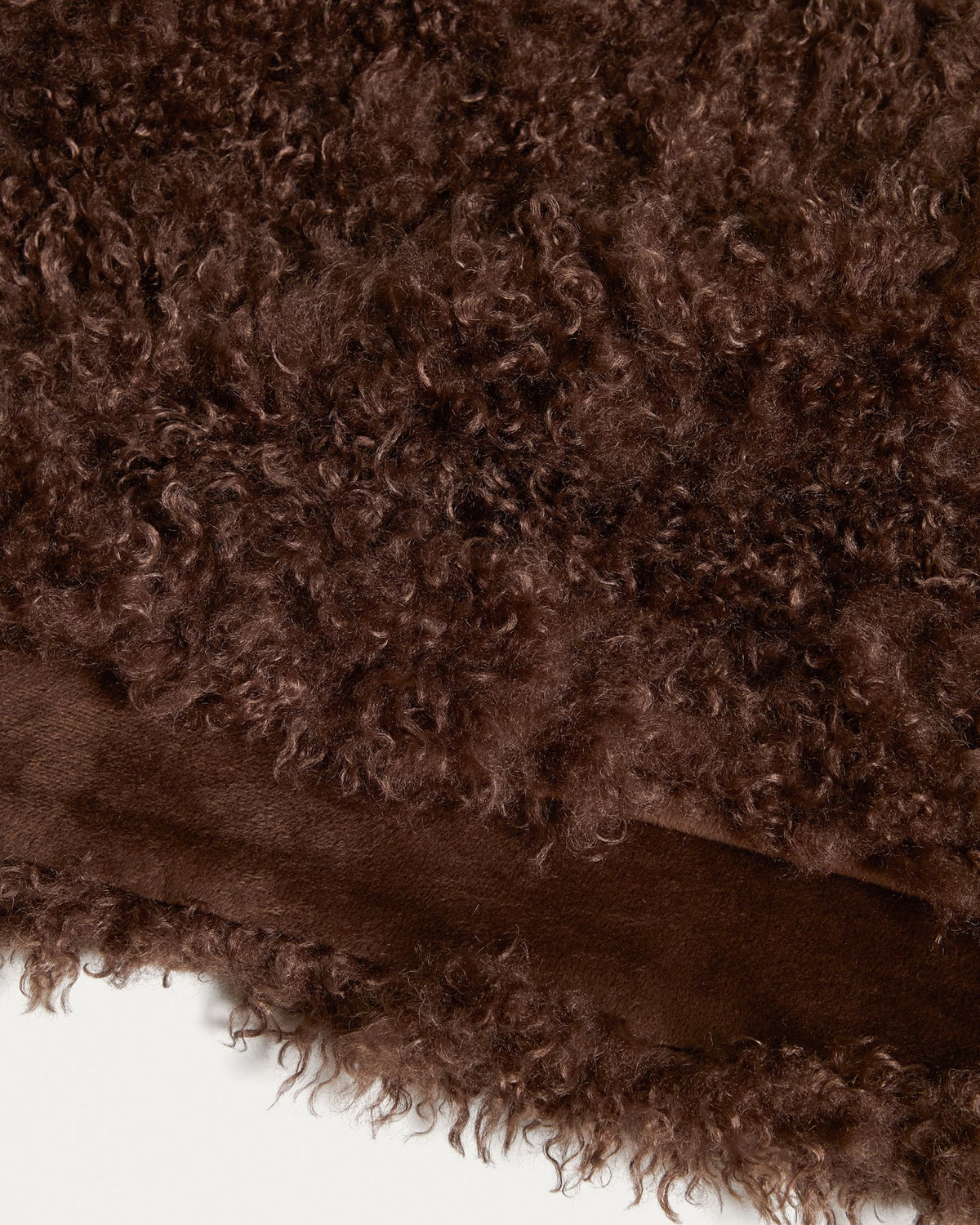 Foto einer schokobraunen Decke aus Kunstfell mit Locken-Optik der Marke Kave Home, Grösse 140 x 200 cm, mit Aufbewahrungsgurt.