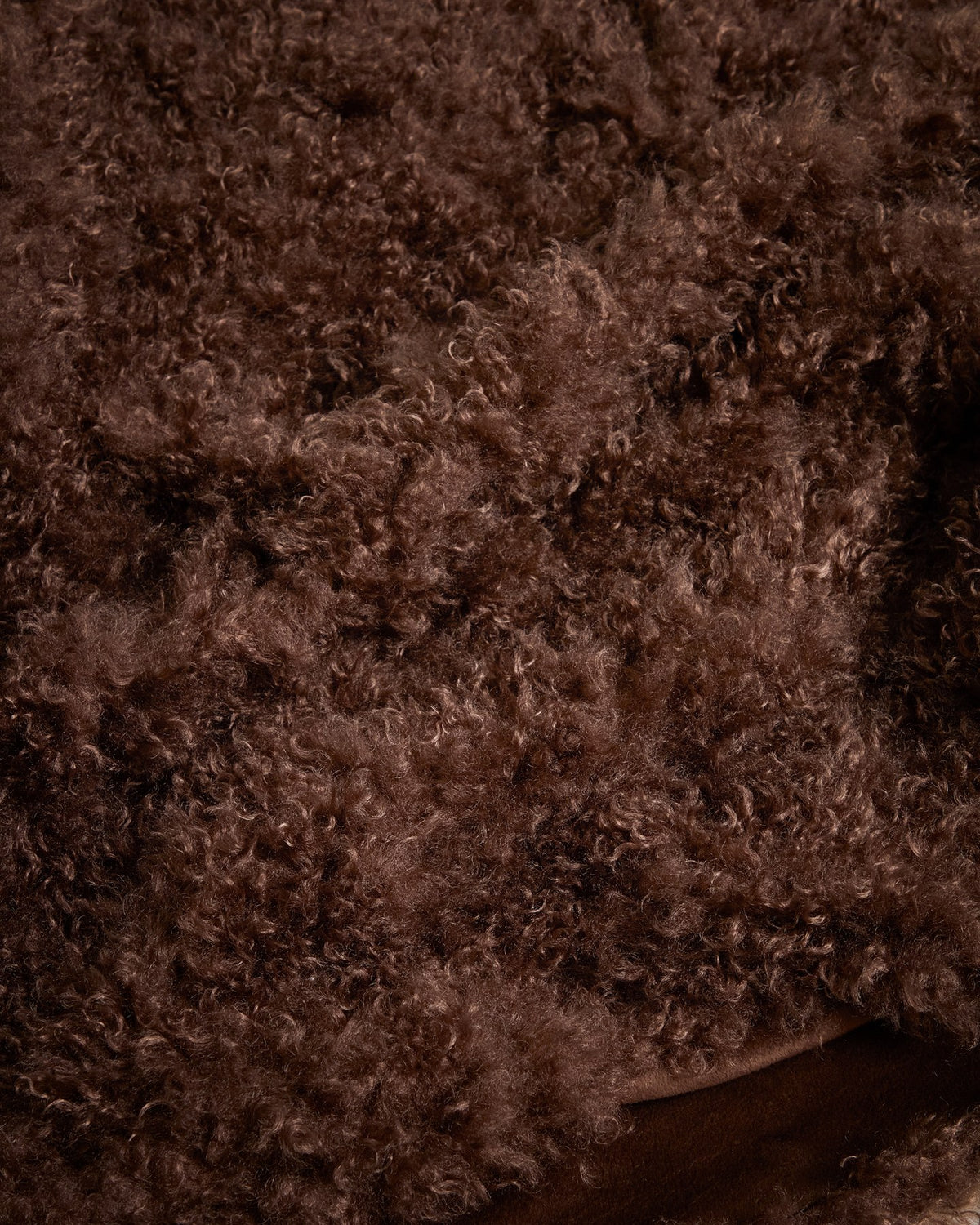Foto einer schokobraunen Decke aus Kunstfell mit Locken-Optik der Marke Kave Home, Grösse 140 x 200 cm, mit Aufbewahrungsgurt.