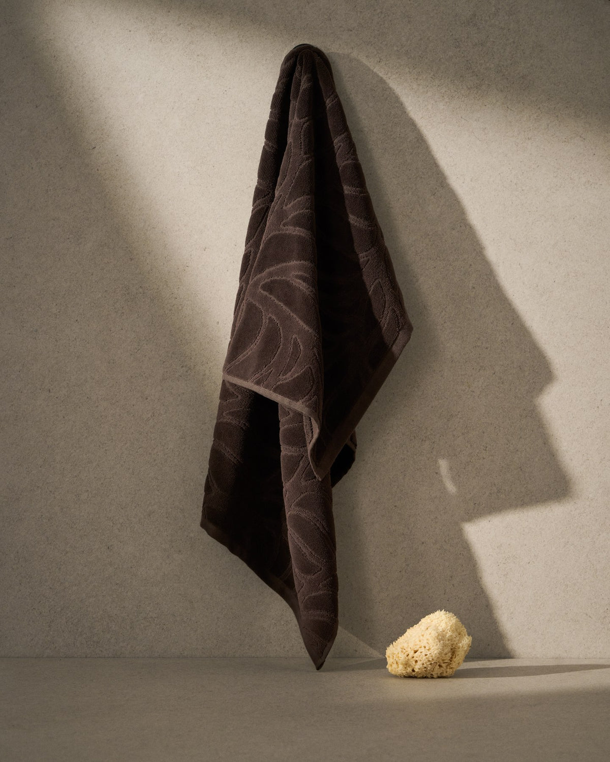 Braunes Handtuch Lurevi aus 100% Baumwolle mit Jacquard-Muster und samtiger Oberfläche, Format 50 x 90 cm, flach ausgebreitet dargestellt.
