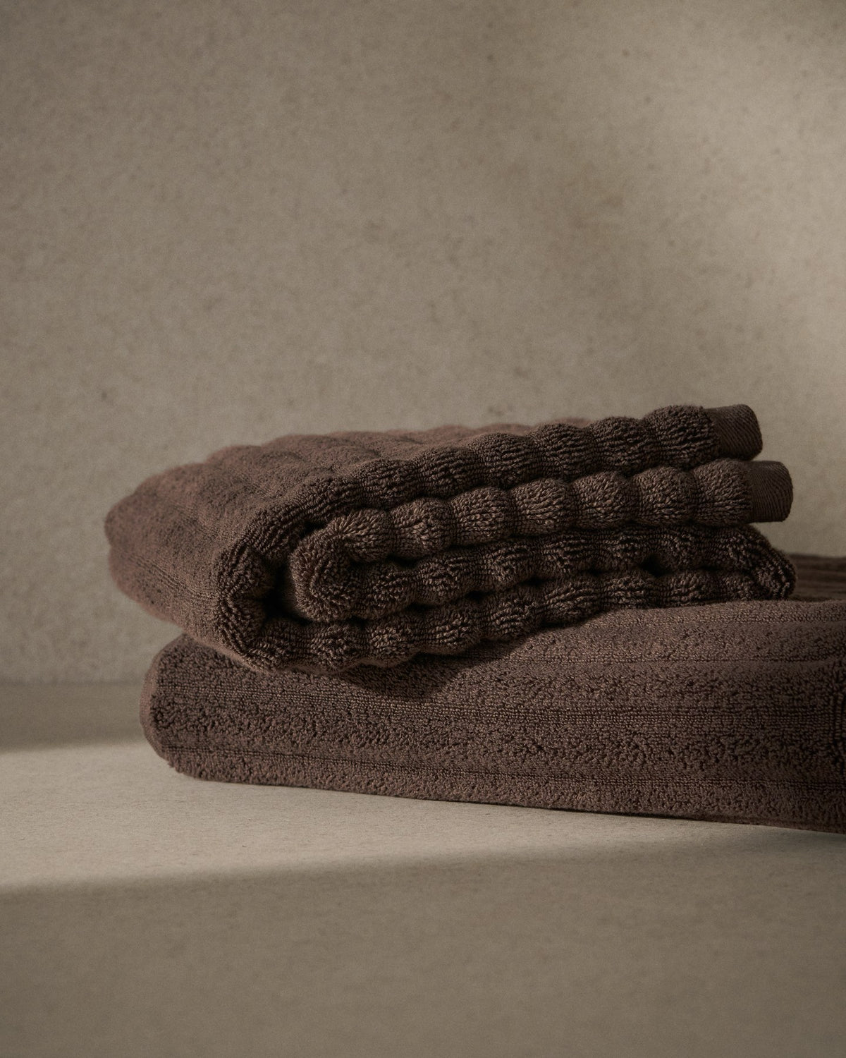 Dunkelbraunes Handtuch aus 100% Baumwolle mit welliger Struktur, rechteckige Form, Masse 50 x 90 cm, liegend fotografiert.