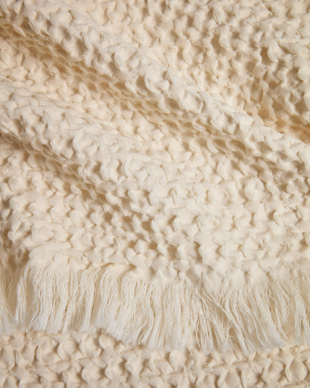 Wolldecke aus 100% Baumwolle mit Waffelstruktur, in der Farbe Ecru, gefaltet dargestellt, Masse 130 x 170 cm, Marke Kave Home.