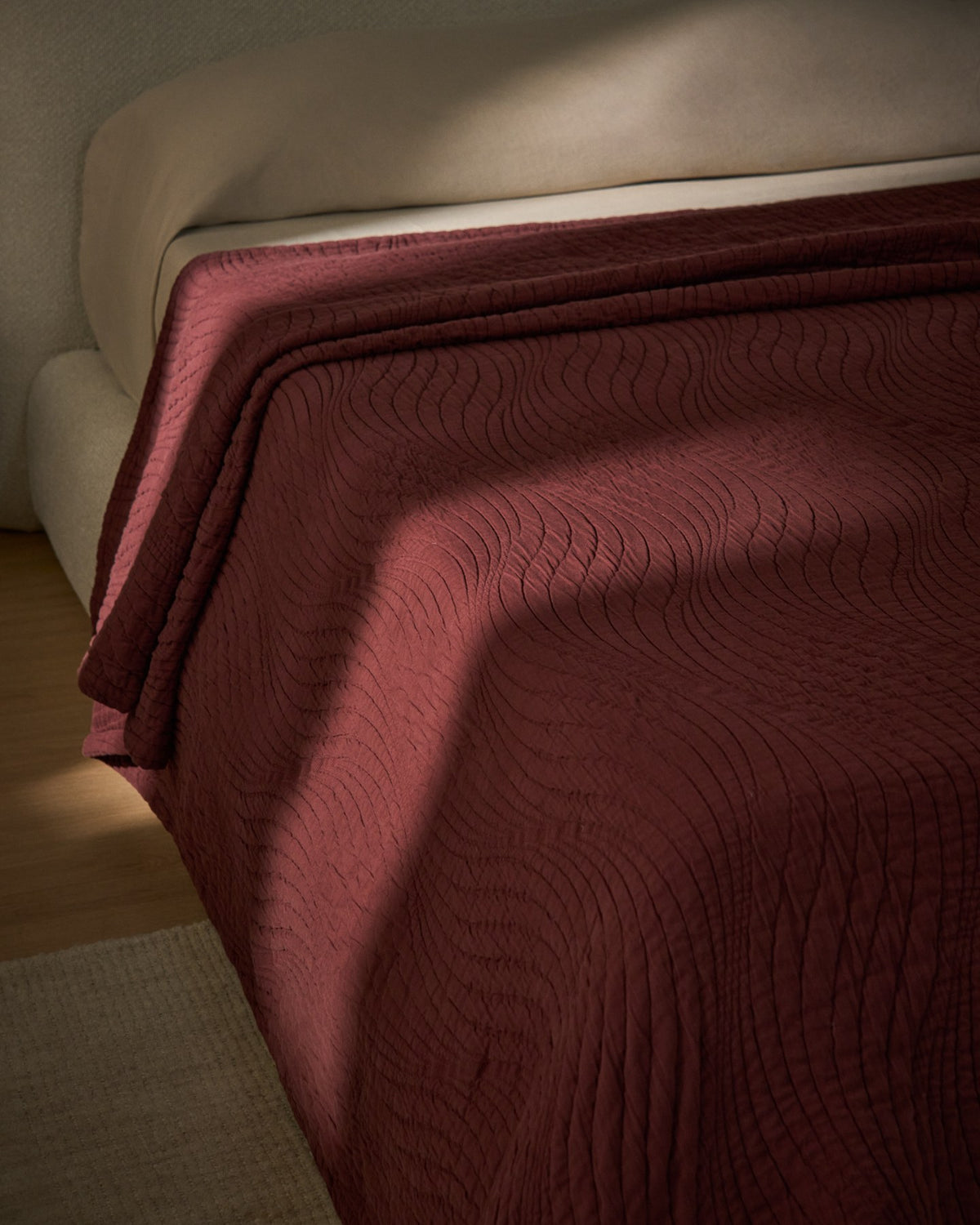 Weinrote Tagesdecke Sarula aus 100% Baumwolle mit Jacquard-Wellenmuster, ausgebreitet auf einem Bett, Grösse 240 x 260 cm.