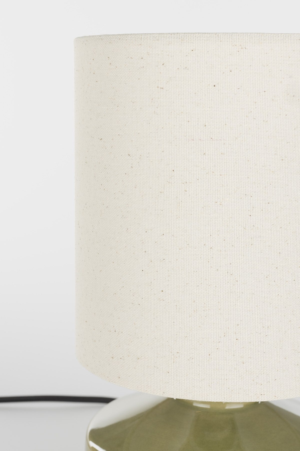 Tischlampe Nook von Zuiver in Grün: runder Lampenschirm aus Leinen auf einem Keramikfuss mit glänzender Oberfläche, Kabel aus schwarzem Textil.